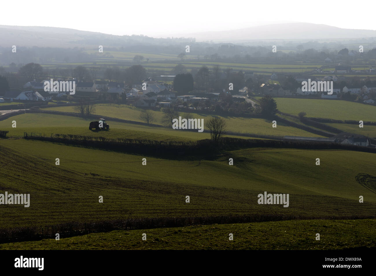 Molla e un agricoltore fatiche in campo con il trattore al di fuori del villaggio in bassa luce misty Foto Stock