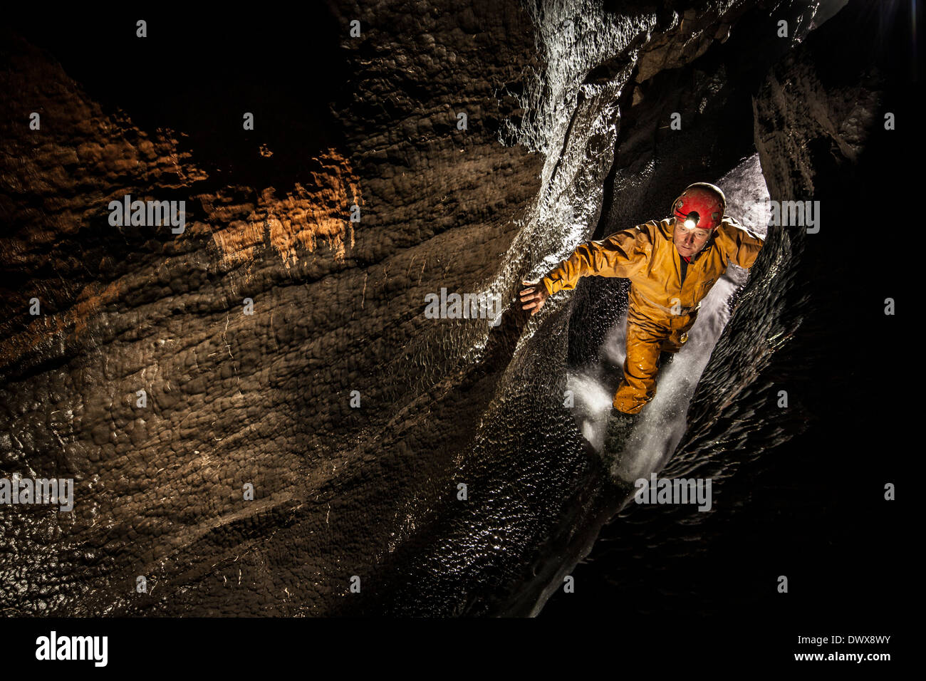 Un speleologo fa la sua strada verso il passaggio del flusso in Ogof Ffynnon Ddu, Brecon Beacons, South Wales, Regno Unito Foto Stock