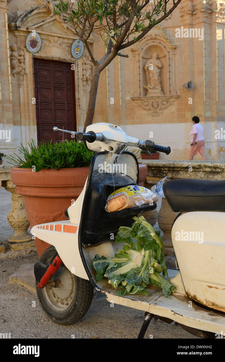 Vecchio motorino scooter con alcuni generi alimentari al di fuori della Chiesa della Visitazione di Gharb. Isola di Gozo. Malta Foto Stock