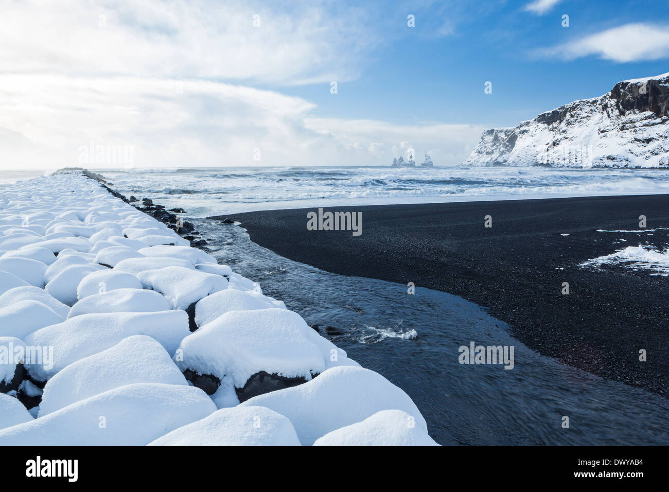 Il basalto nero sabbie e un molo di roccia ricoperti di neve fresca a Vík í Mýrdal sulla costa sud dell'Islanda Foto Stock