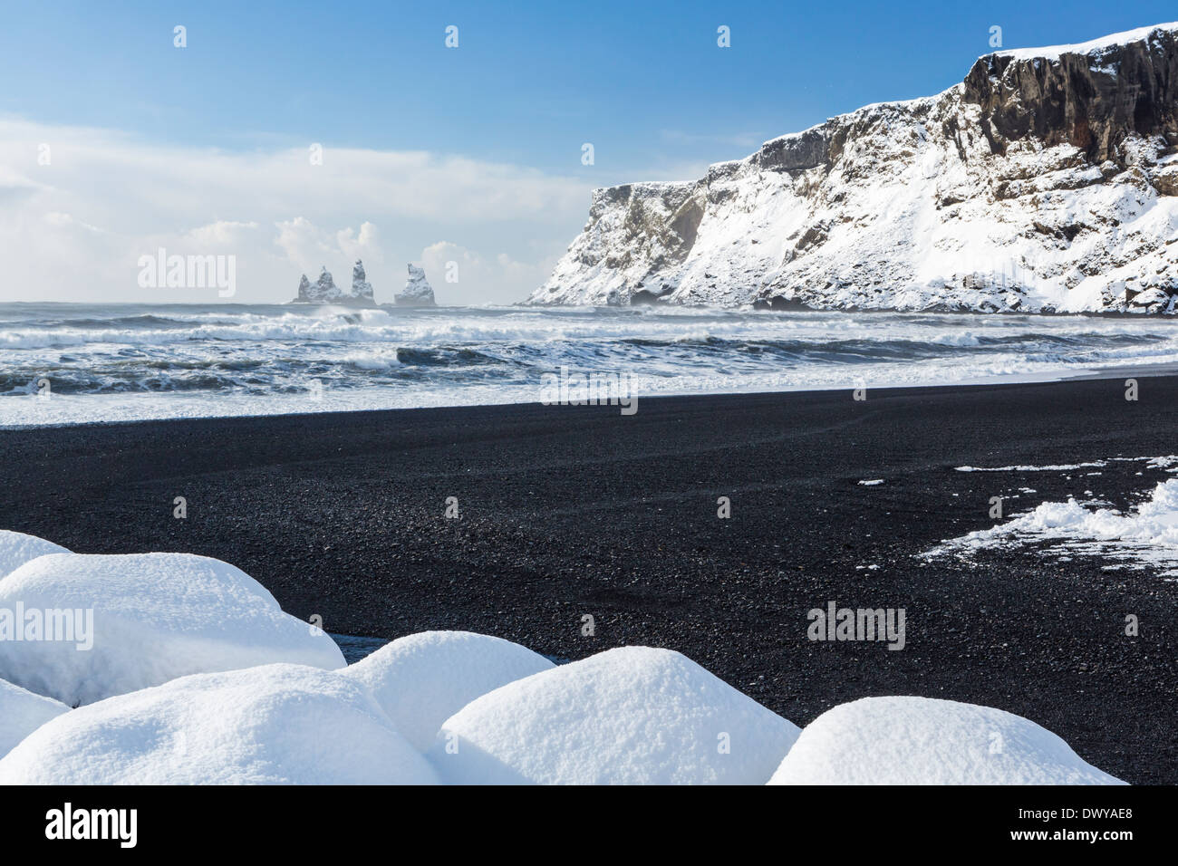 Il basalto nero sabbie e un molo di roccia ricoperti di neve fresca dopo una tempesta in Vík í Mýrdal sulla costa sud dell'Islanda Foto Stock