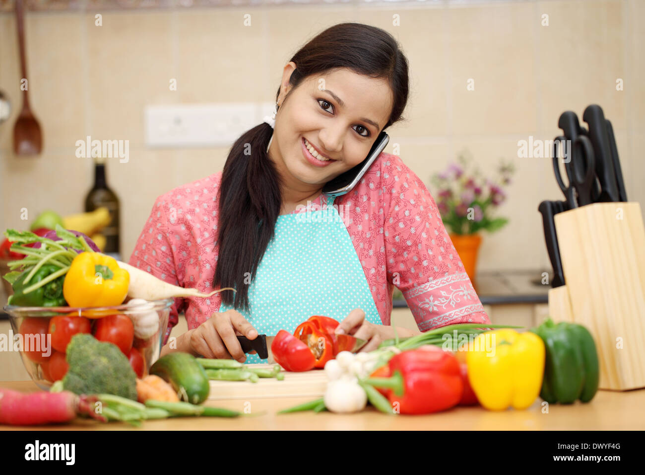 Sorridente giovane donna il taglio di verdure e parlando al cellulare Foto Stock