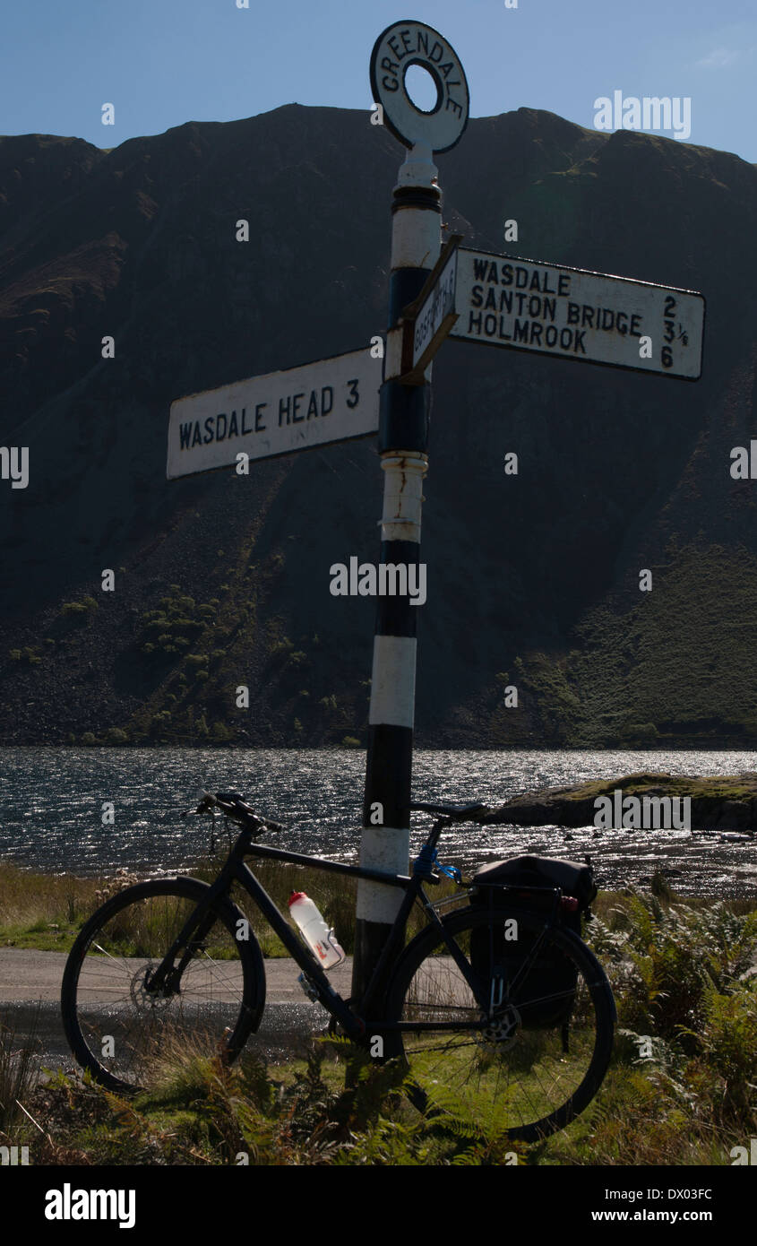 Un nero touring bike in appoggio contro una direzione road post da Wastwater lago nel distretto del lago, Cumbria, Inghilterra Foto Stock