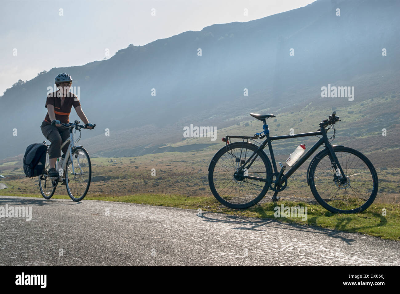 Un ciclista femmina si avvicina a un parcheggiato touring bike sulla strada stretta di Mungrisedale, Lake District, Inghilterra Foto Stock