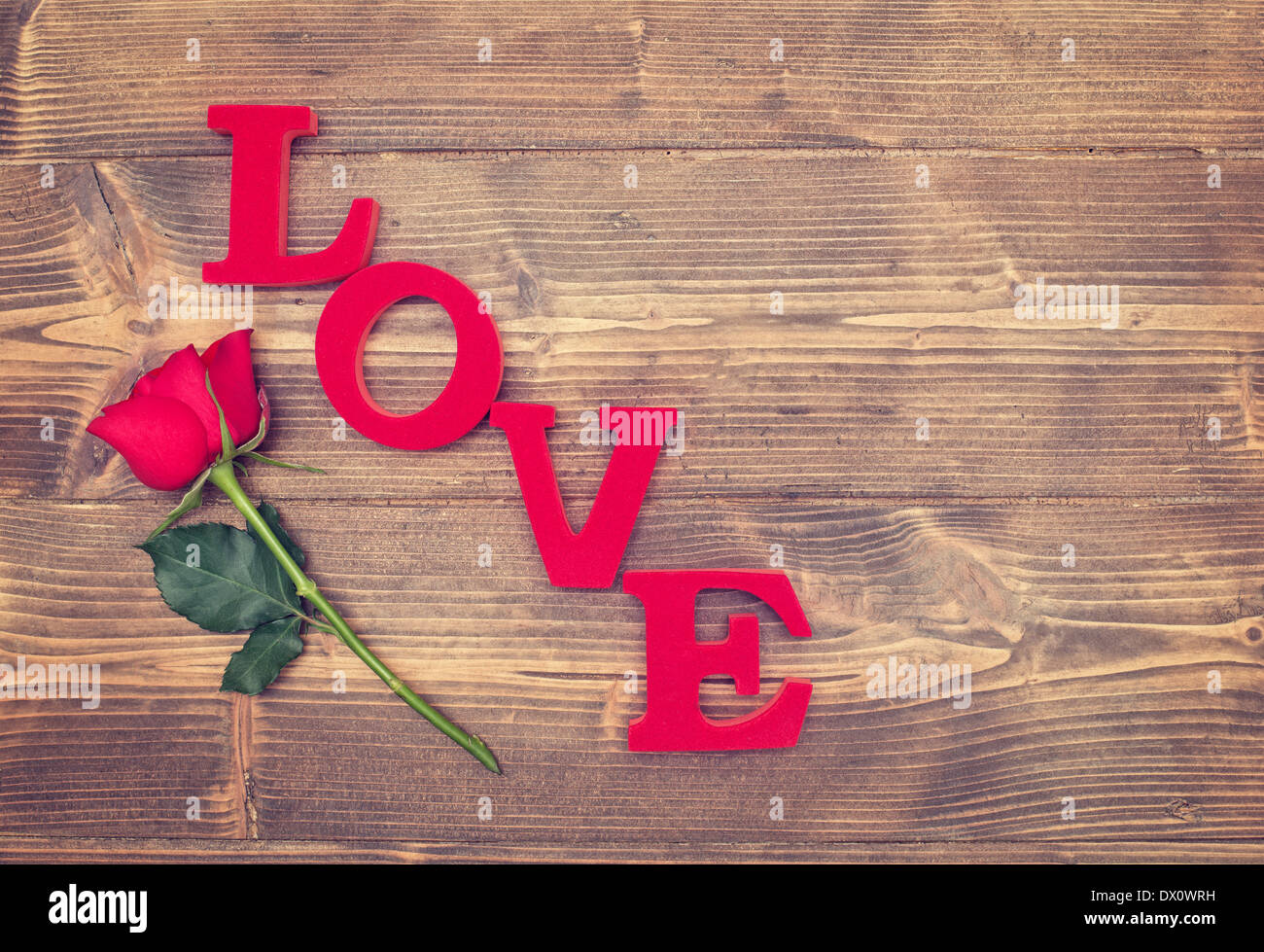 Single red rose e la parola amore su un sfondo rustico Foto Stock