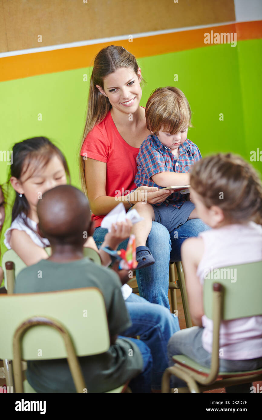 I bambini in una scuola materna seduti in cerchio e la lettura di libro con insegnante di vivaio Foto Stock