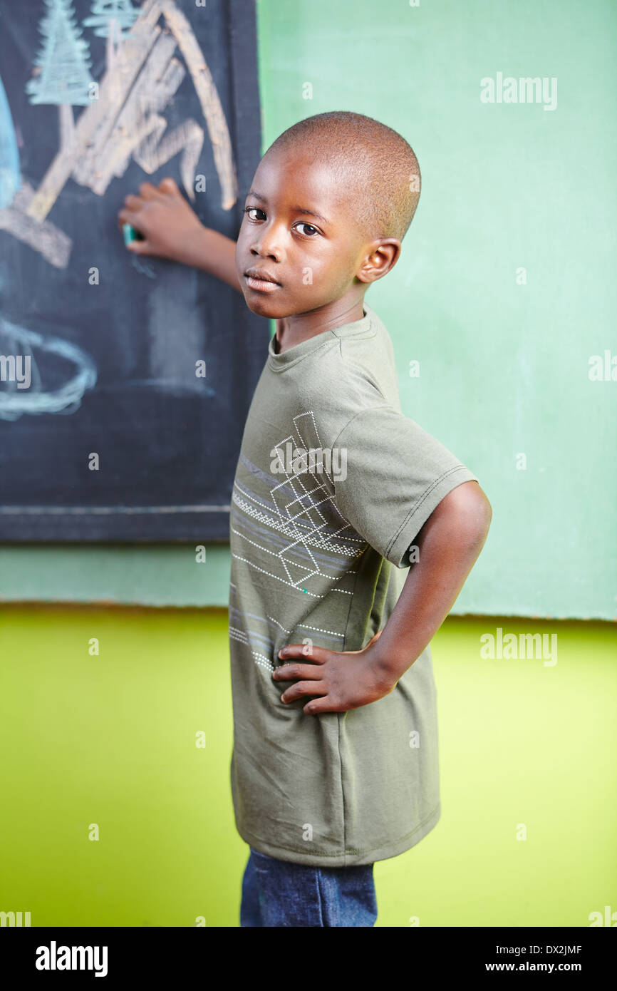 Bambino africano con un gessetto sulla lavagna in un kindergarten Foto Stock