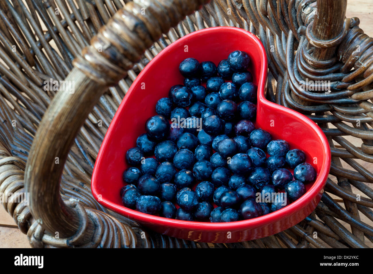 I mirtilli salute del cuore dello Shopping basket cibo sano concetto / i mirtilli in un cuore rosso piatto sagomato in un tradizionale cesto in vimini Foto Stock