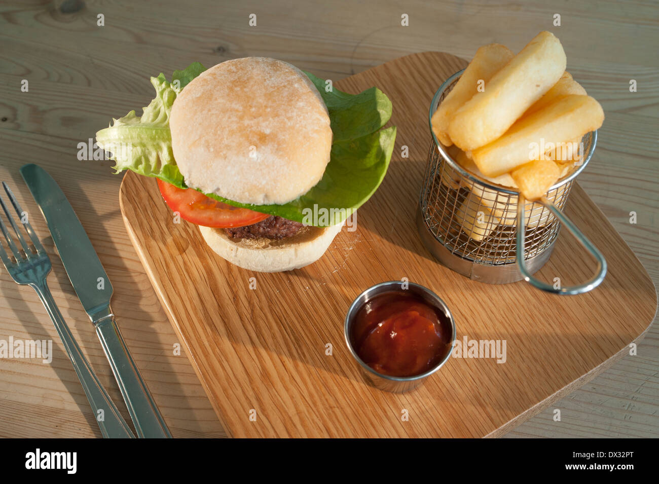 Burger con un contorno di insalata in un pane bianco bun con un ordine di patatine fritte e ketchup servita su un piatto di legno Foto Stock