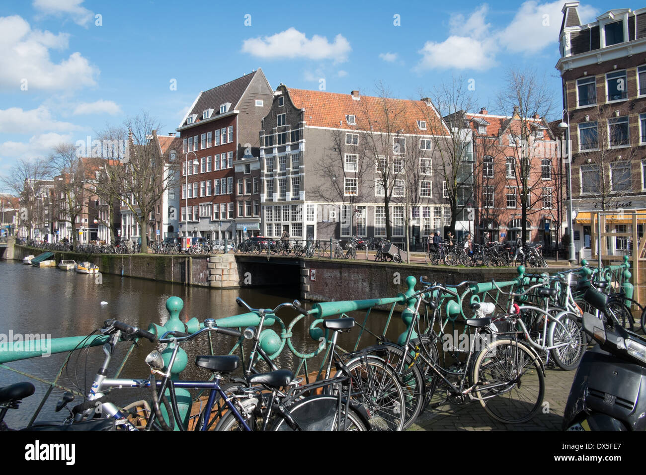 Biciclette incatenato ad un ponte sul canale accanto a un certo numero di Amsterdam tradizionali case di città e ex magazzini, Amsterdam Foto Stock