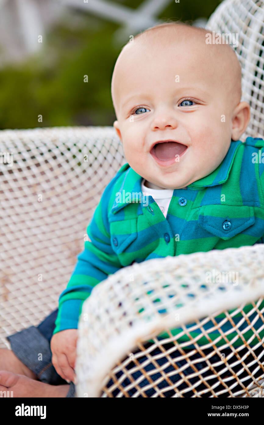 Laughing baby boy con la bocca aperta nel filo sedia, guardando lontano Foto Stock
