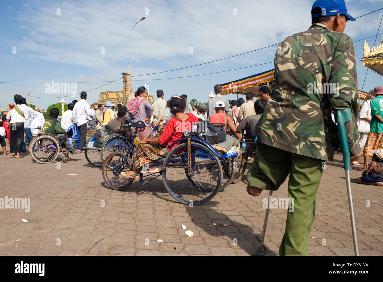 Un handicap uomo amputato è camminare con le stampelle vicino a persone disabili confinato su una sedia a rotelle in Phnom Penh Cambogia. Foto Stock