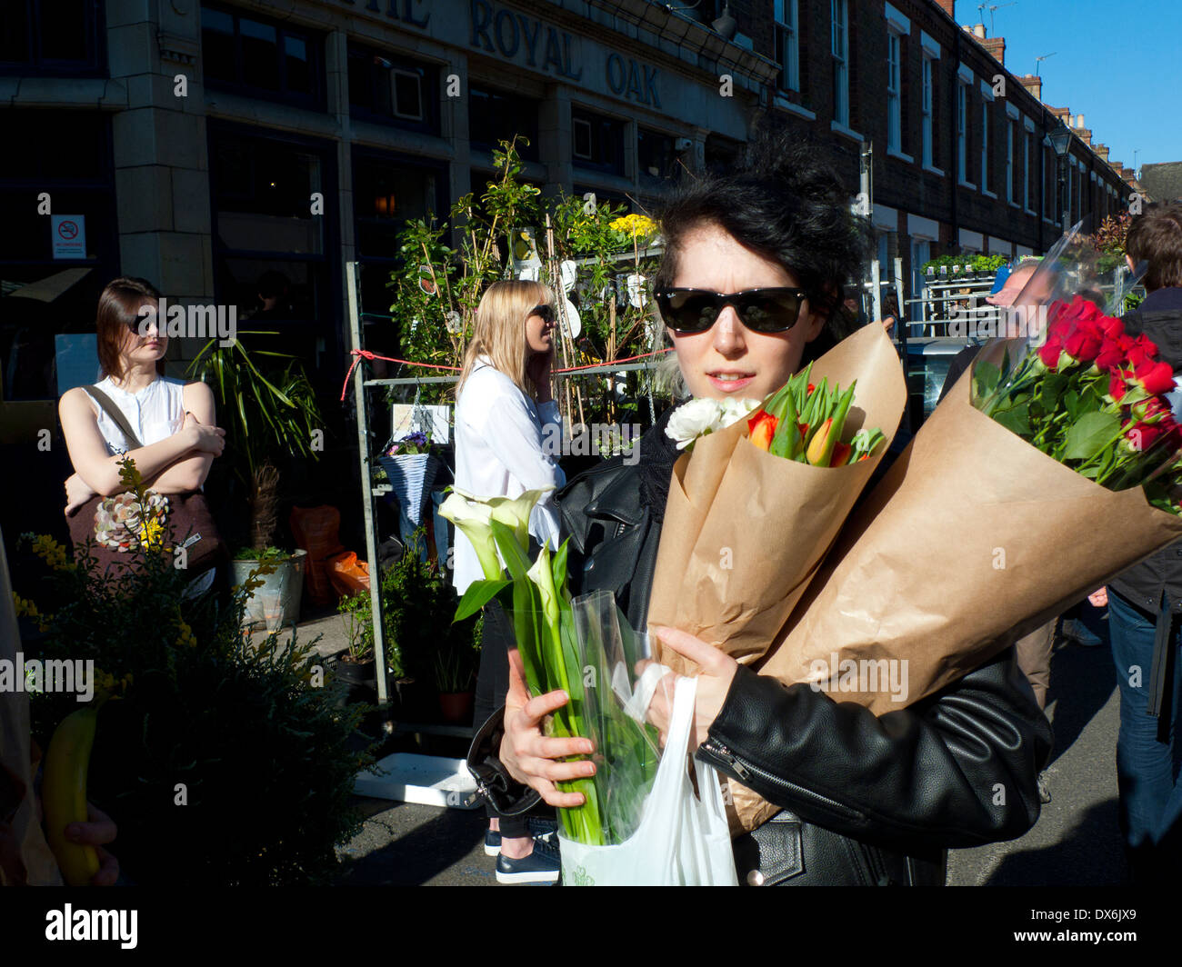 Donna impianto di trasporto Acquisto di piante tulipani gigli rose rosse a piedi lungo la strada nel sole a Columbia Road Flower Market London E2 UK KATHY DEWITT Foto Stock