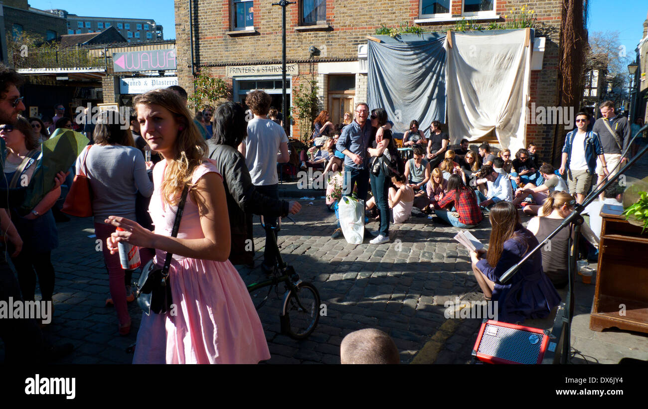 Donna in un abito rosa che cammina in una folla di persone sedute al panificio Jones in Ezra Street Columbia Road Flower Market London E2 Inghilterra UK KATHY DEWITT Foto Stock