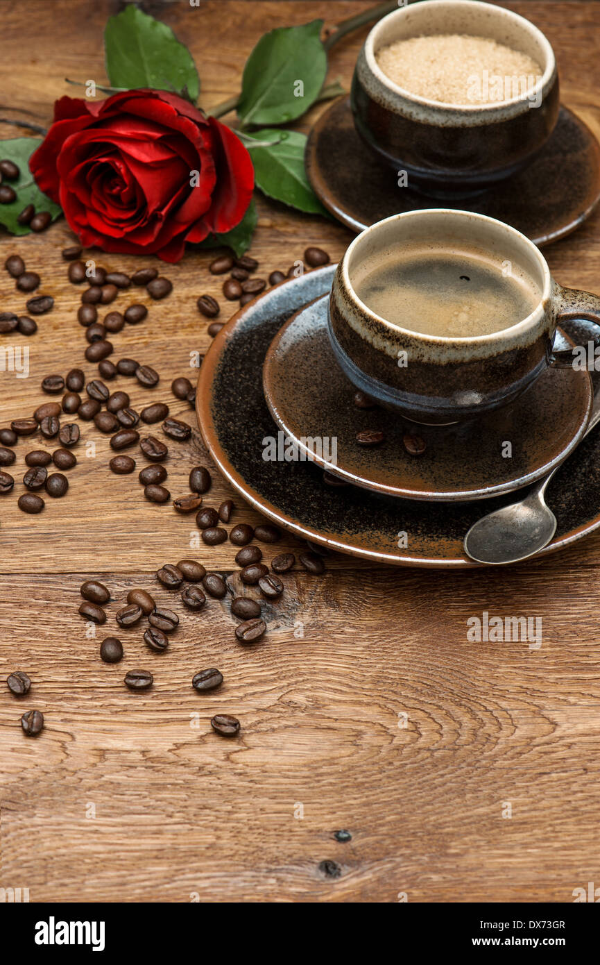 Tazza di caffè nero e rosso fiore rosa su sfondo di legno. Disposizione di festa Foto Stock