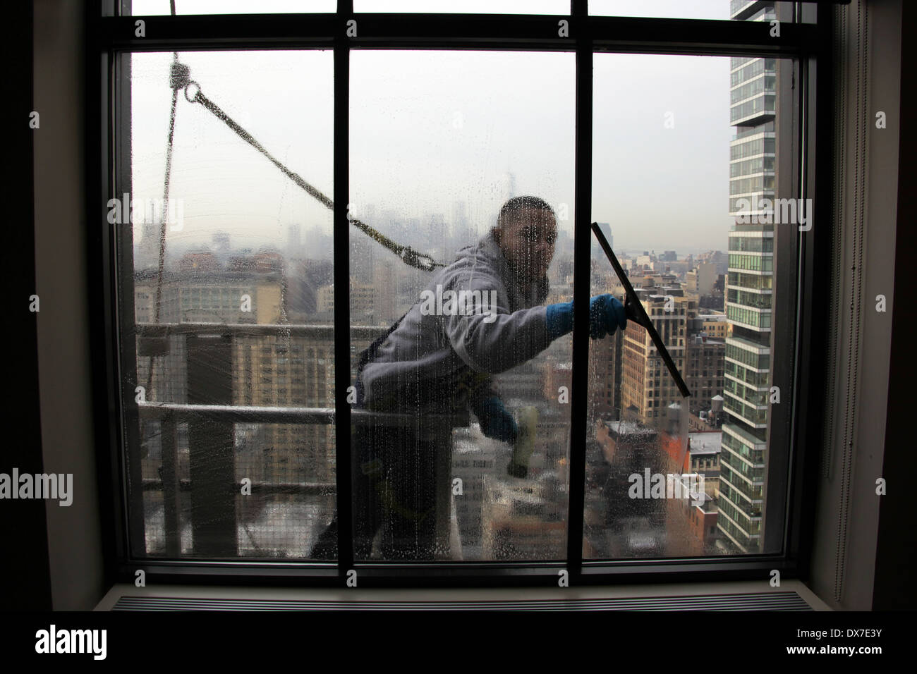 Vista interna di una finestra la rondella in piedi sul ponteggio e fissato mediante cablaggio durante la pulizia di una New York City grattacielo windows Foto Stock
