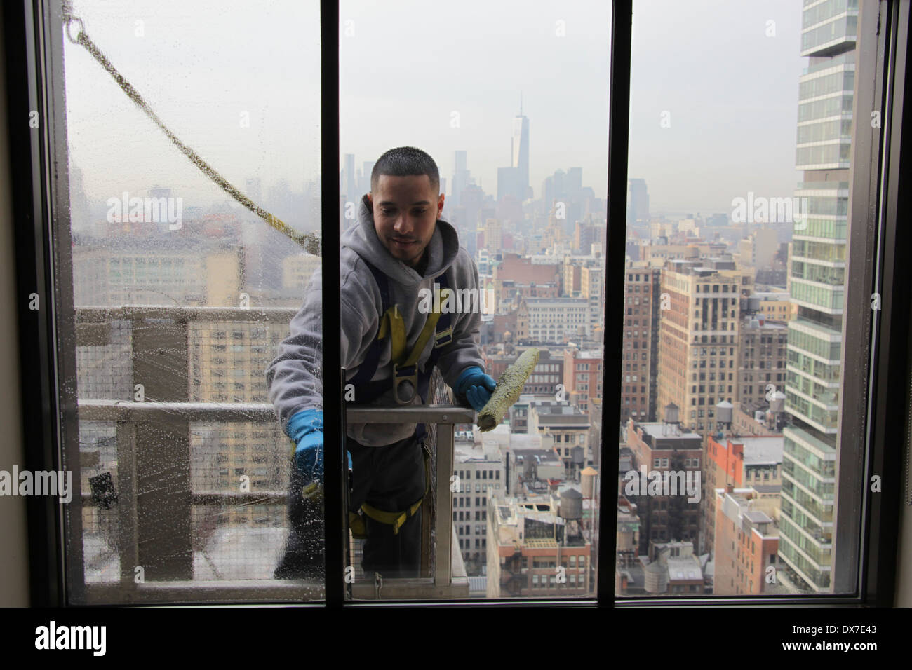 Vista interna di una finestra la rondella in piedi sul ponteggio e fissato mediante cablaggio durante la pulizia di una New York City grattacielo windows Foto Stock
