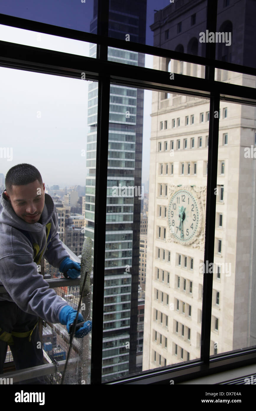 Vista interna di una finestra la rondella in piedi sul ponteggio e fissato mediante cablaggio durante la pulizia di una New York City grattacielo windows Foto Stock