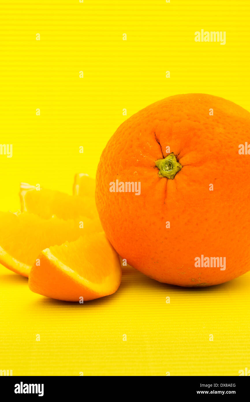 Uno tutta arancione e quattro fette accanto ad esso con uno sfondo giallo. Arance noti per la loro elevata fonte di vitamina C. Foto Stock