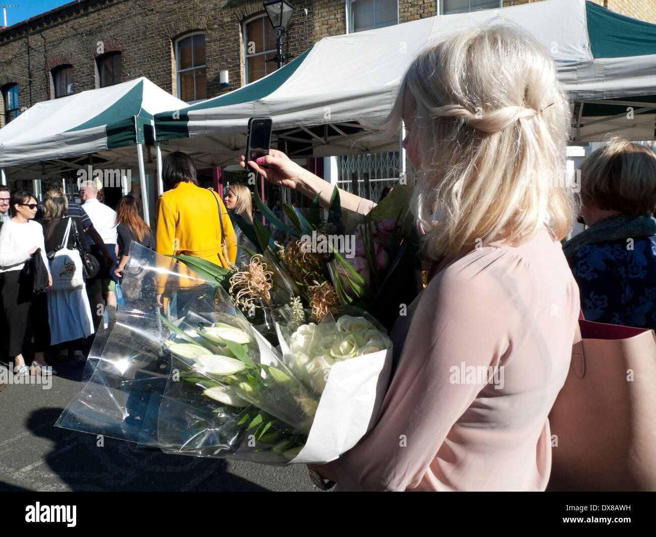 Donna che mantiene le fotografie dei gigli selfie con telefono cellulare presso la Columbia Road Flower Market London E2 UK KATHY DEWITT Foto Stock