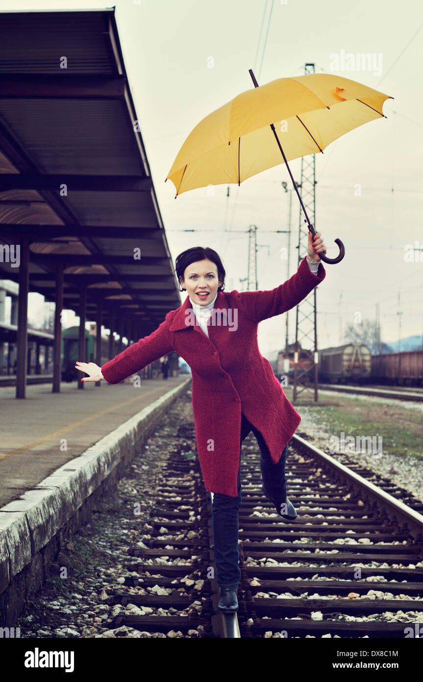 Donna in equilibrio su una gamba in piedi sul binario ferroviario tenendo ombrello Foto Stock