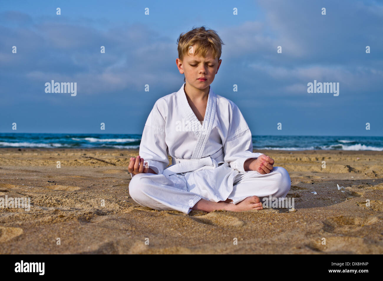 Un ragazzo in un kimono medita sulla spiaggia. Sullo sfondo di un cielo e mare Foto stock Alamy