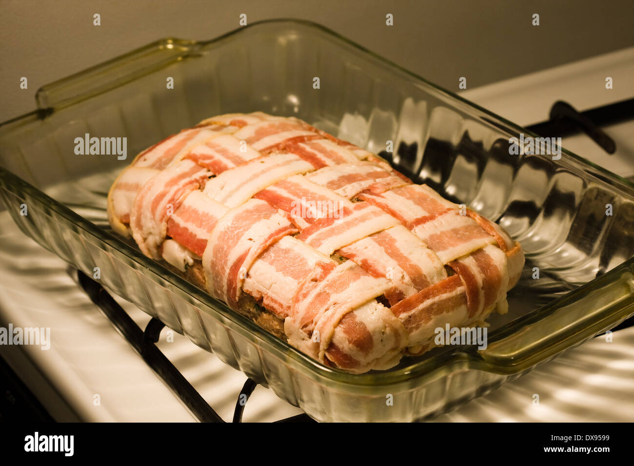 Polpettone crudo avvolto con il bacon in una cesta modello di armatura seduto in un chiaro in Pyrex teglia su una cucina piano cottura Foto Stock