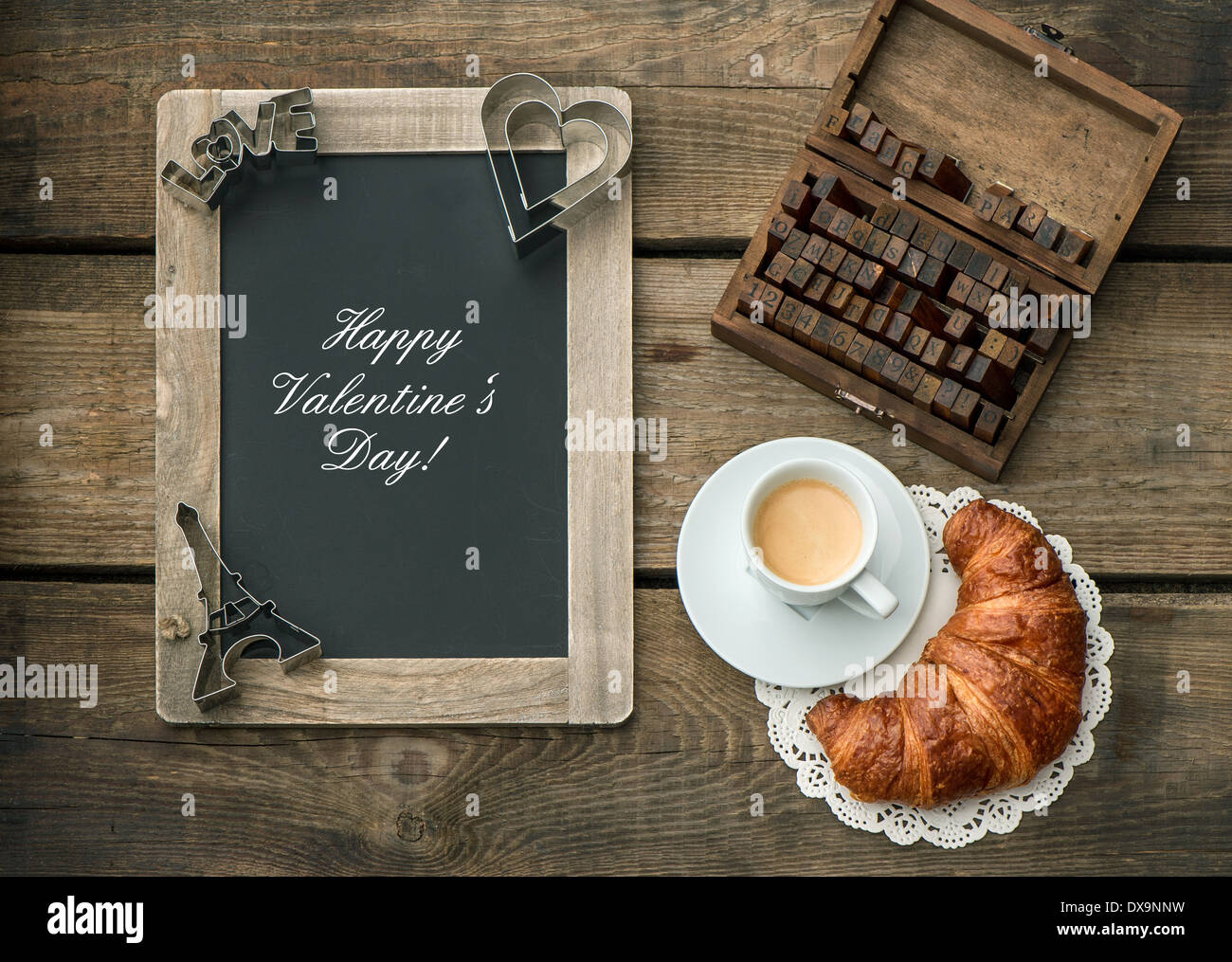 Tazza di caffè nero con croissant, lavagna e decorazione di cuore su rustiche in legno. sfondo romantico San Valentino breakfast o Foto Stock