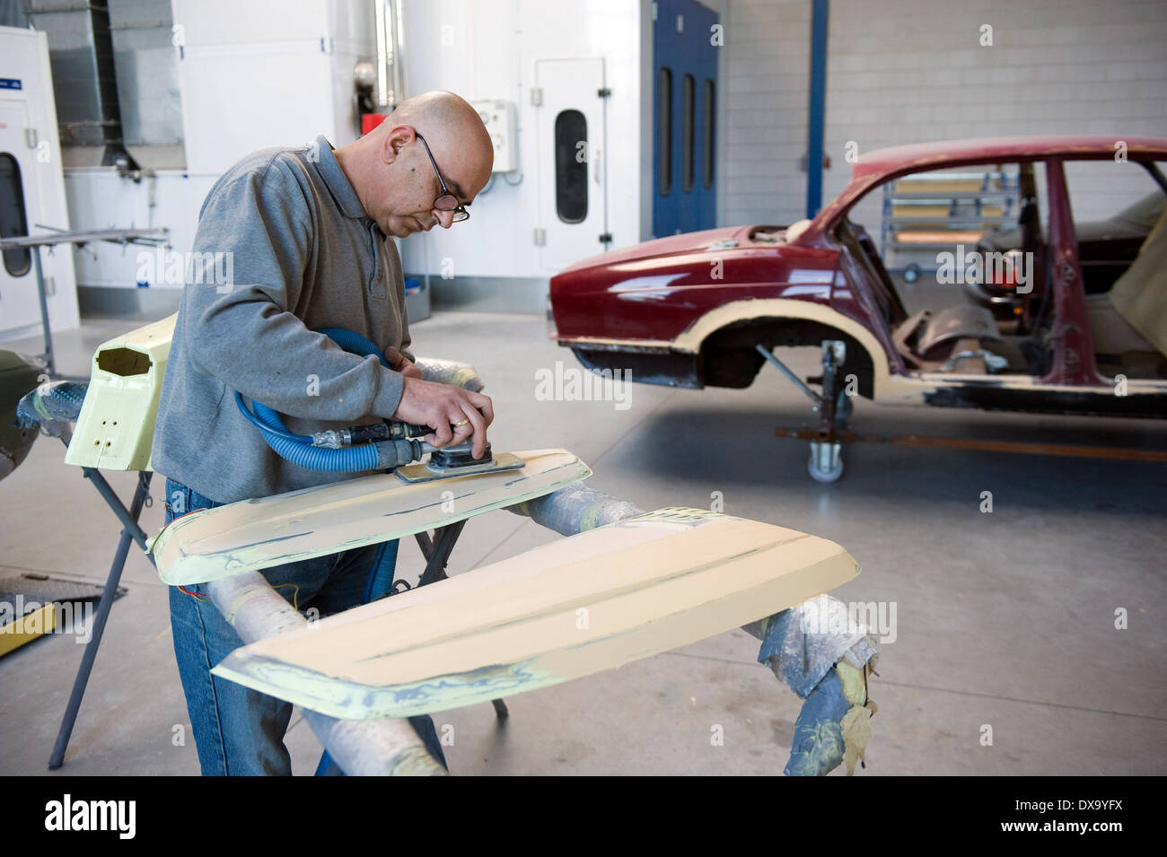 Una vettura repairman sta preparando una parte di una cassa per la riverniciatura in un garage Foto Stock