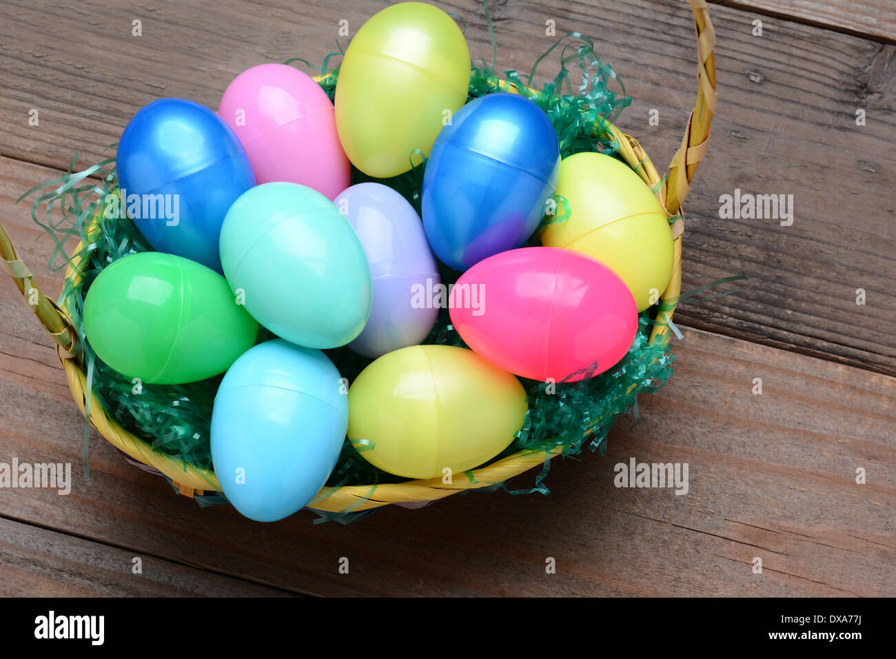 Elevato angolo di visione di un cestello riempito con plastica colorate uova di Pasqua. Formato orizzontale su di un legno rustico sfondo. Foto Stock