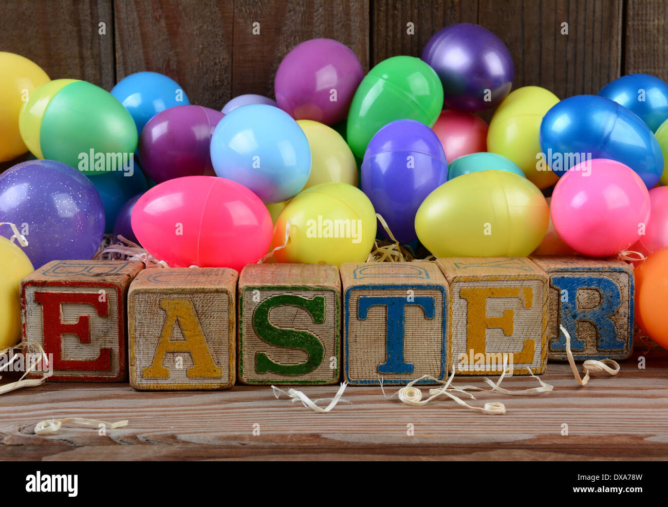 La parola Pasqua enunciato nel giocattolo per bambini blocchi e un mucchio di uova in plastica. Formato orizzontale su di un legno rustico sfondo. Foto Stock