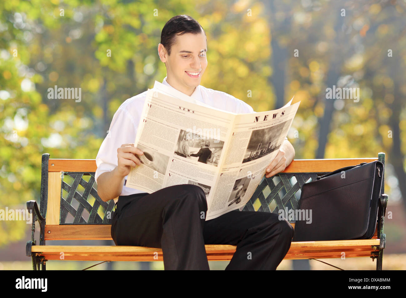 Imprenditore seduto su una panca in legno la lettura di un quotidiano in un parco Foto Stock