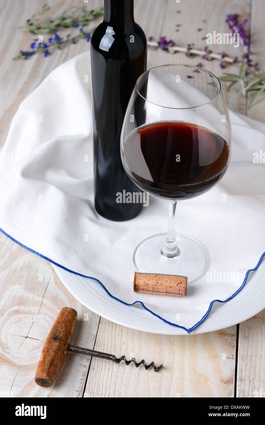 Elevato angolo di vino fiore e ancora in vita. Bicchiere di vino rosso e una bottiglia su un asciugamano e legno tavolo rustico. Formato verticale. Foto Stock