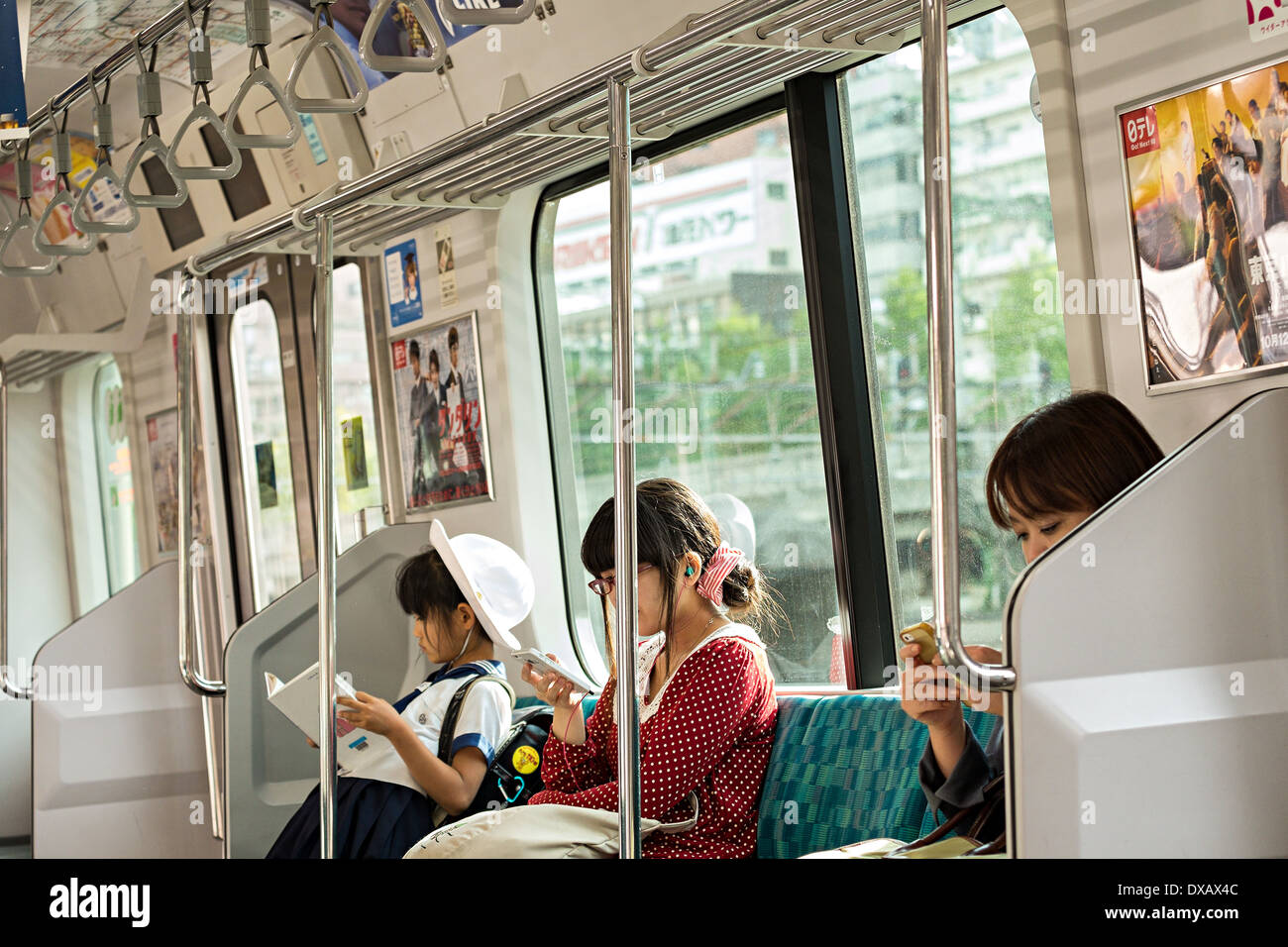 Un giovane giapponese schoolgirl leggendo un libro e 2 donne giapponesi pendolari la lettura di telefoni cellulari a Tokyo in treno, Tokyo, Giappone Foto Stock