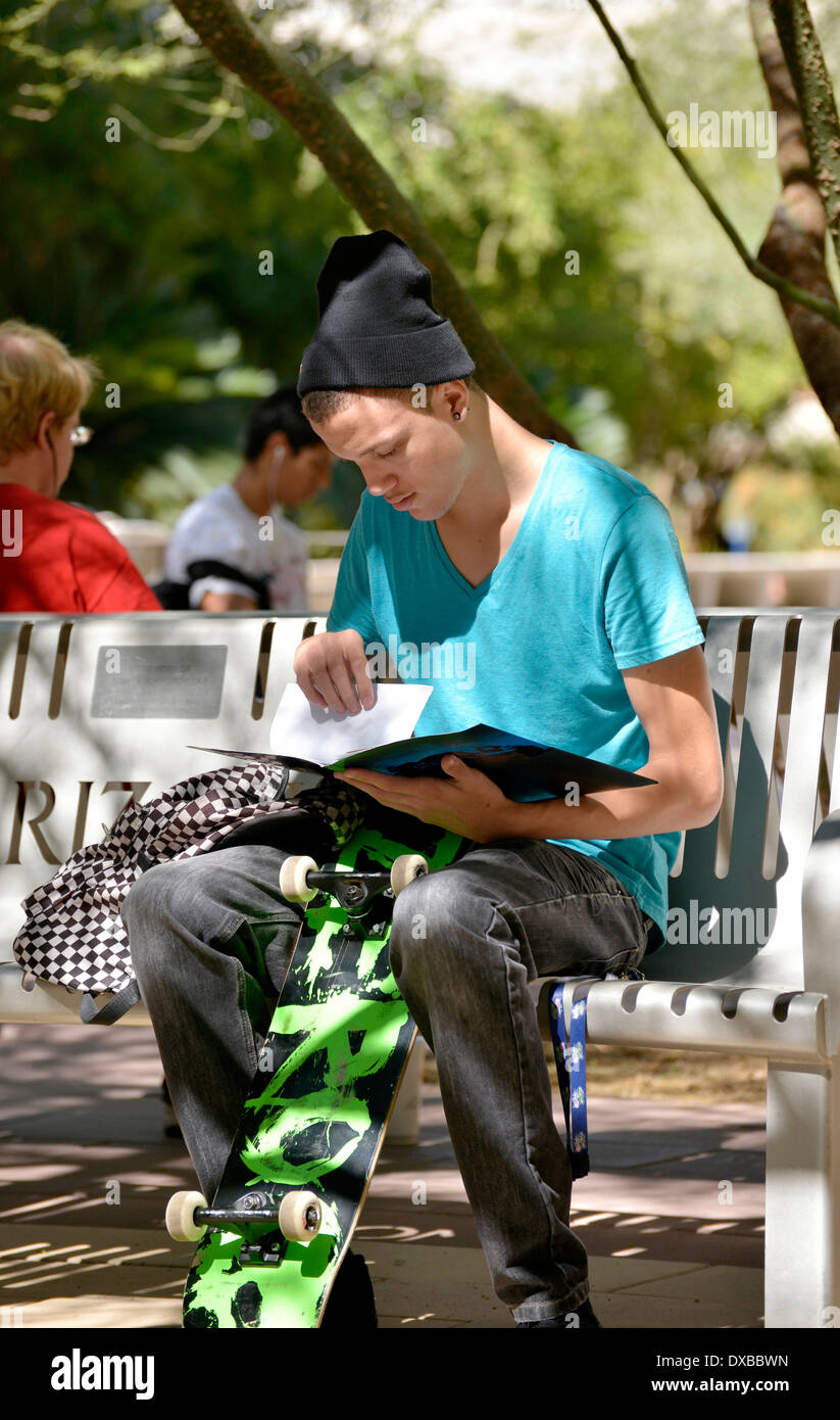 Un giovane uomo su un campus universitario cercando attraverso opuscoli educativi. Foto Stock