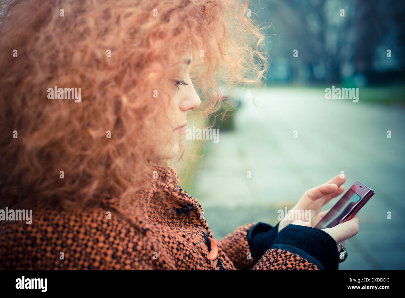 Giovane bella rossa di capelli ricci donna utilizzando il cellulare al parco Foto Stock