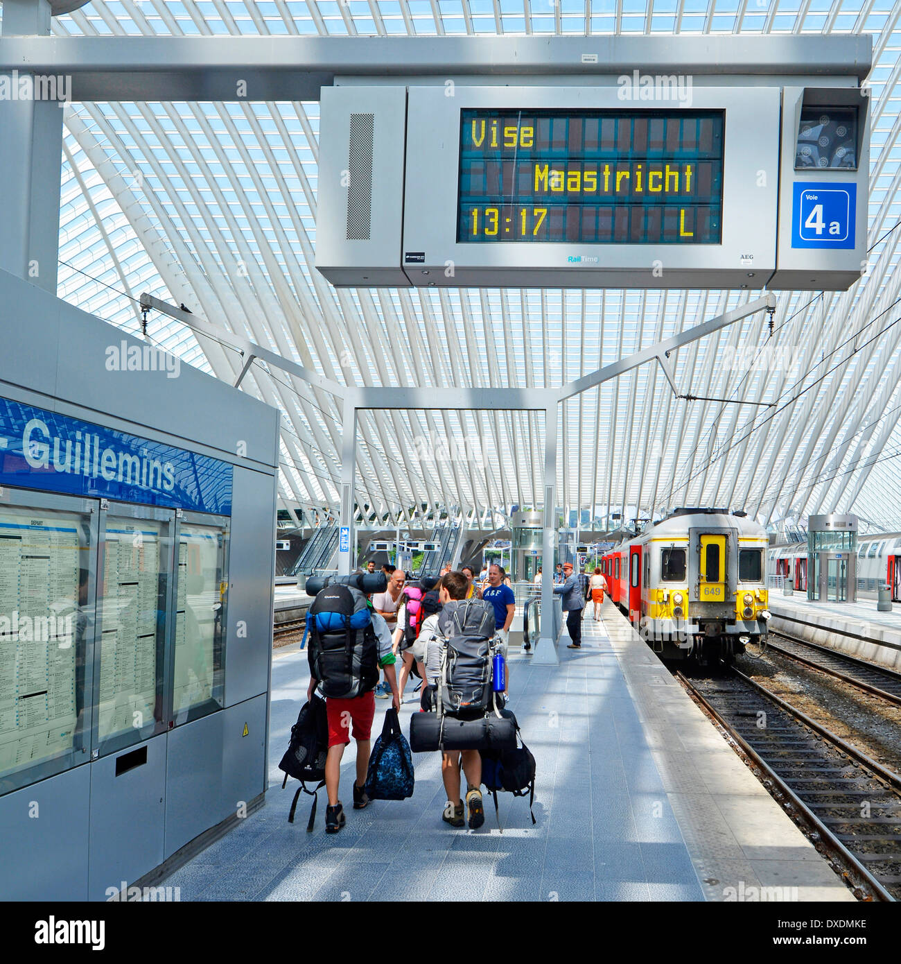 Backpackers gruppo stazione ferroviaria piattaforma caricata con kit zaino in moderno trasporto pubblico tetto di vetro edificio scheda partenze Belgio Liege Foto Stock