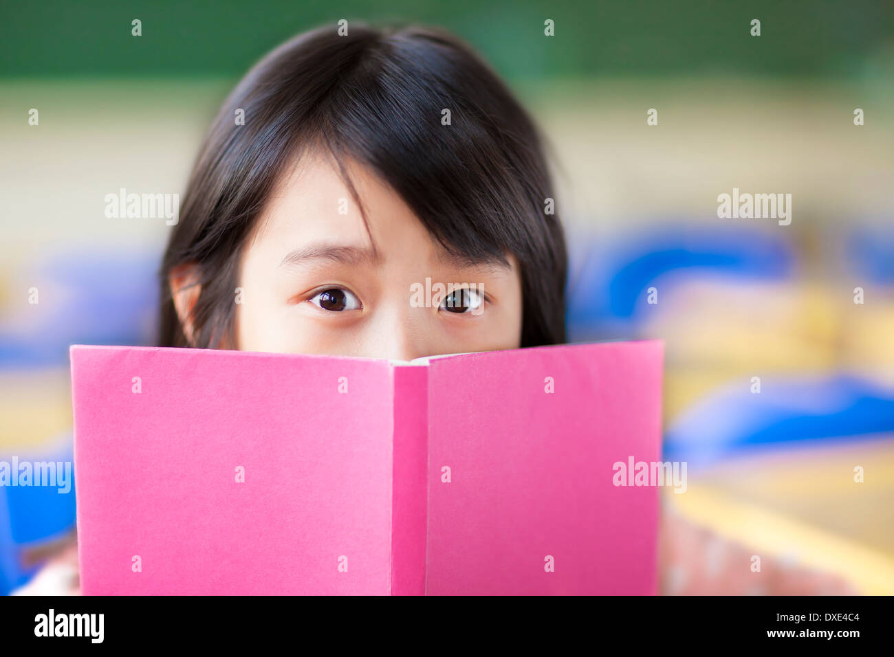 Ragazza utilizza un libro per coprire il suo volto in aula Foto Stock