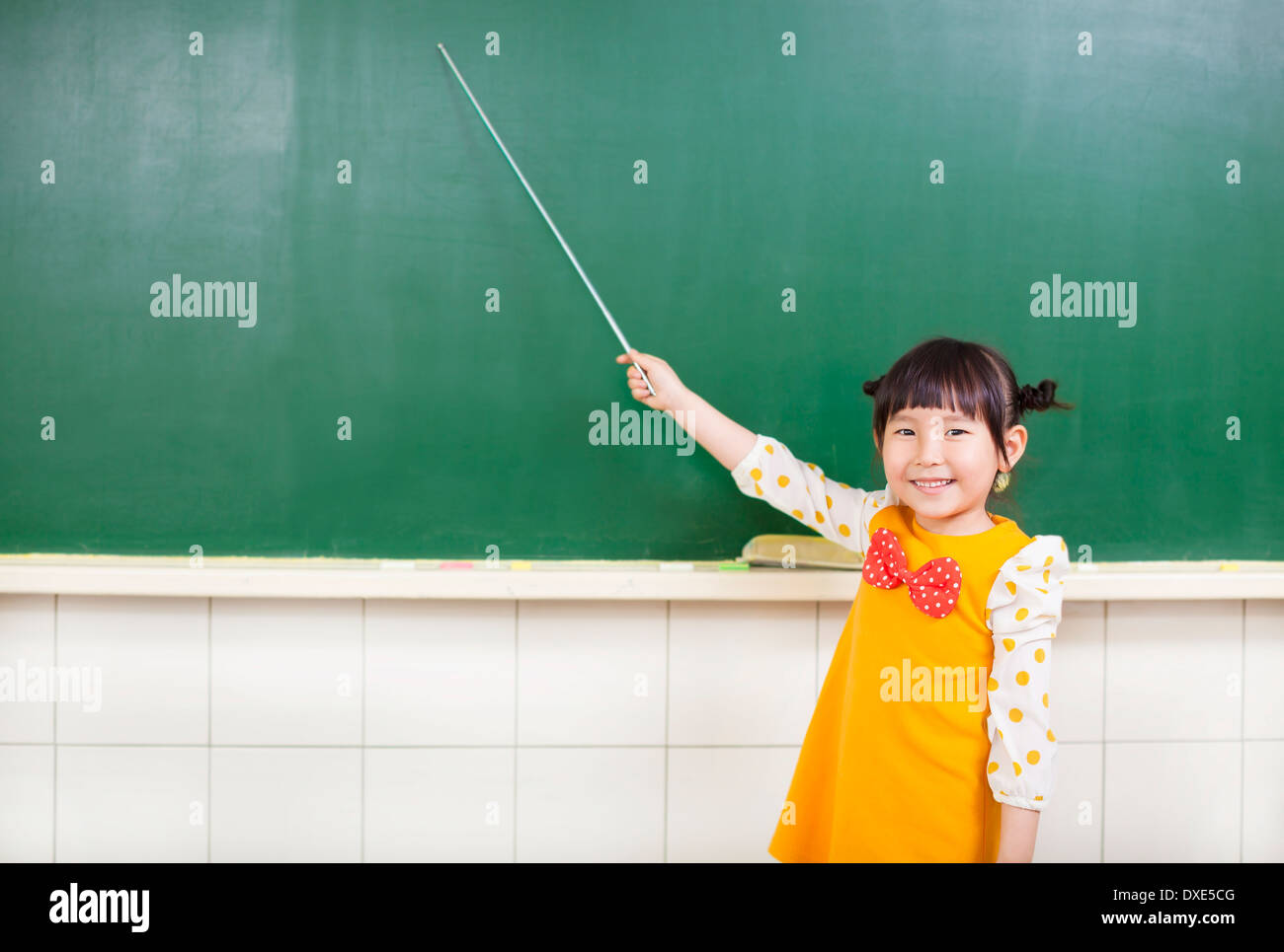 Bambina utilizzando una bacchetta di puntare su una lavagna in aula Foto Stock