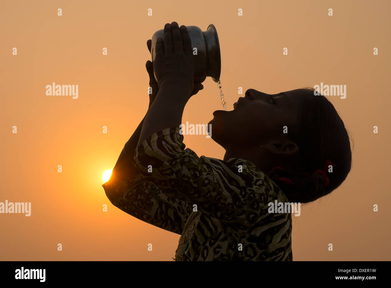 India, Uttar Pradesh, Agra,silhouette della ragazza di bere dalla brocca al tramonto. Foto Stock