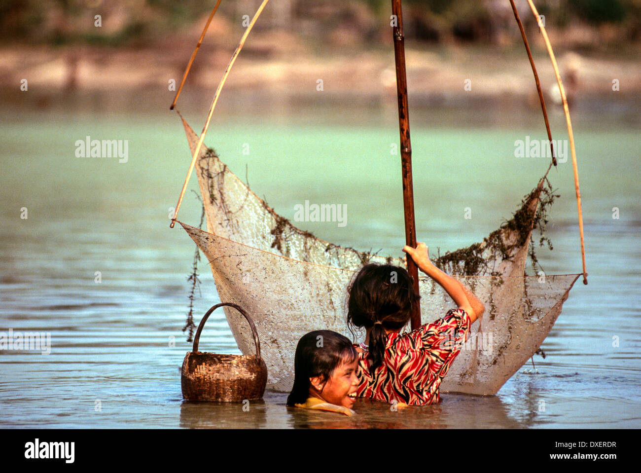 Laos bambini rete da pesca poli di bambù riverbank alberi sunshine fiume blu piscina di acqua Foto Stock