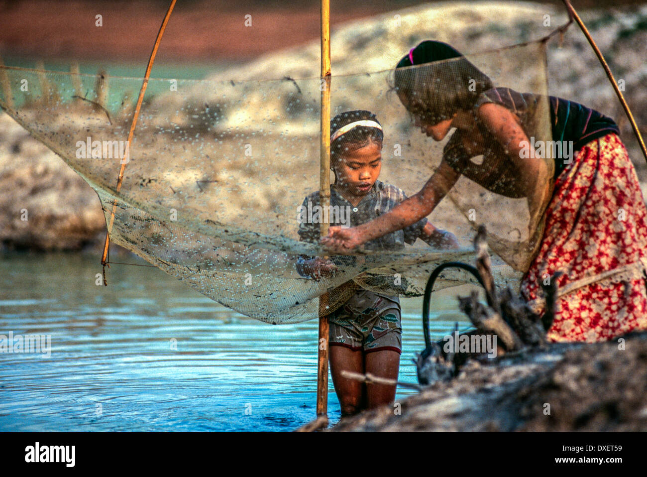 Laos bambini rammendo rete da pesca poli di bambù riverbank alberi sunshine fiume acqua blu Ragazzi Ragazze Foto Stock