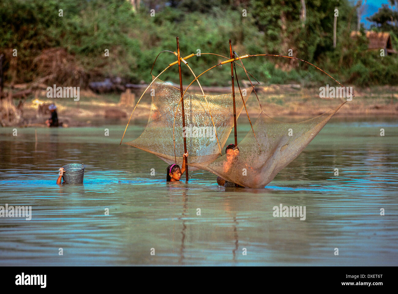 Laos donna rete da pesca poli di bambù blue sky riverbank soffici nuvole alberi sunshine fiume cesto tessuto floating Foto Stock