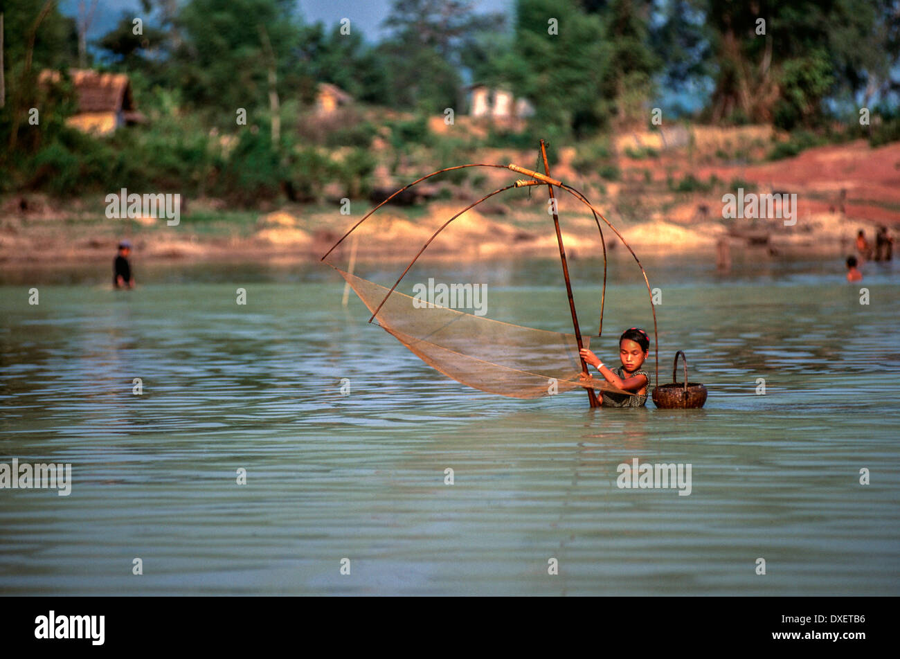 Laos donna rete da pesca poli di bambù blue sky riverbank soffici nuvole alberi sunshine fiume cesto tessuto floating Foto Stock