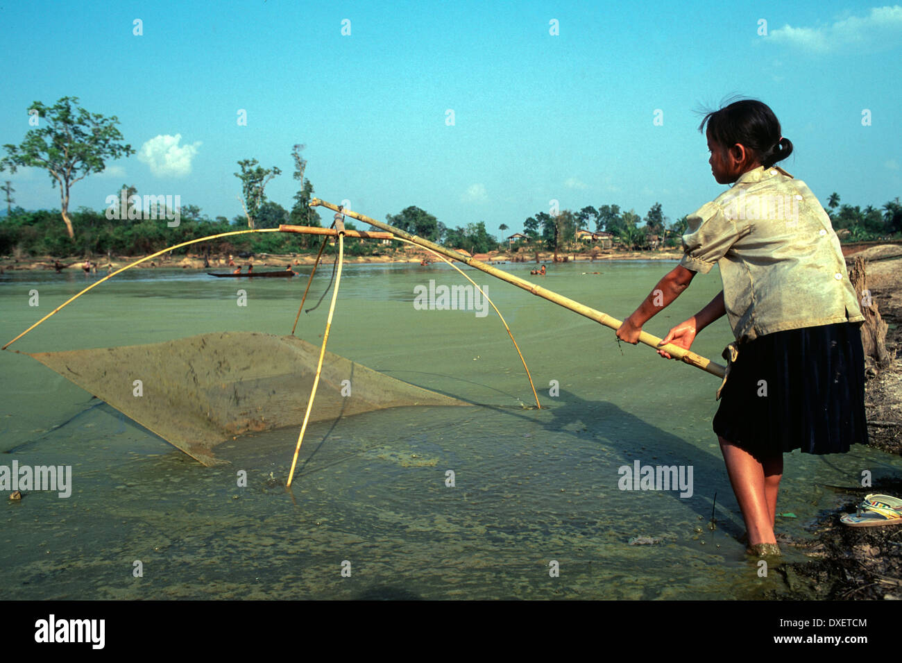 Laos donna rete da pesca poli di bambù blue sky riverbank soffici nuvole sole alberi Foto Stock