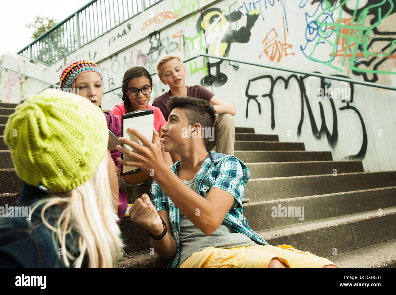 Un gruppo di bambini seduti sulle scale all'aperto, utilizzando i computer tablet e smartphone, Germania Foto Stock