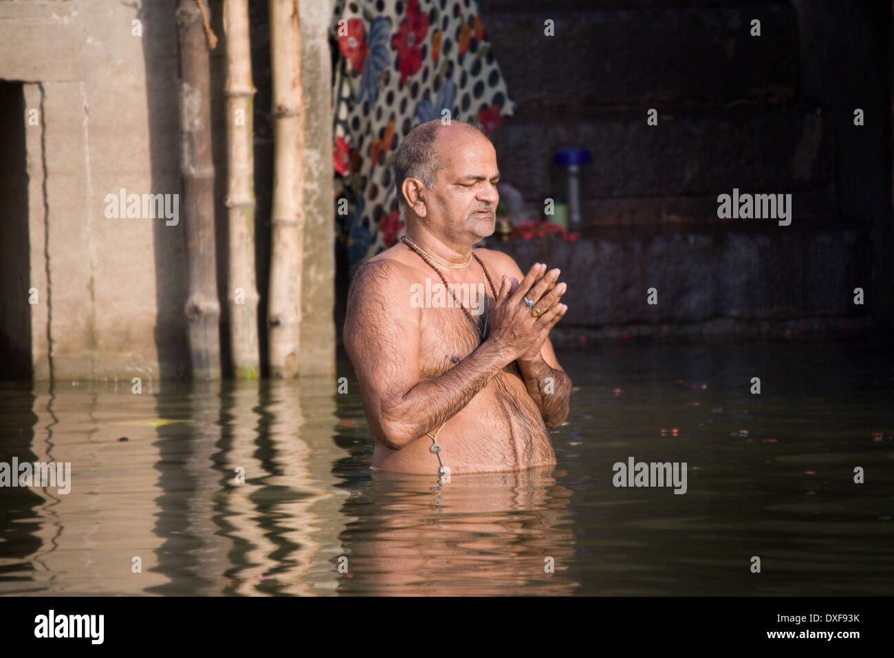 Uomo indù in preghiera e il bagno rituale al ghats indù sulle rive del fiume sacro Gange Foto Stock