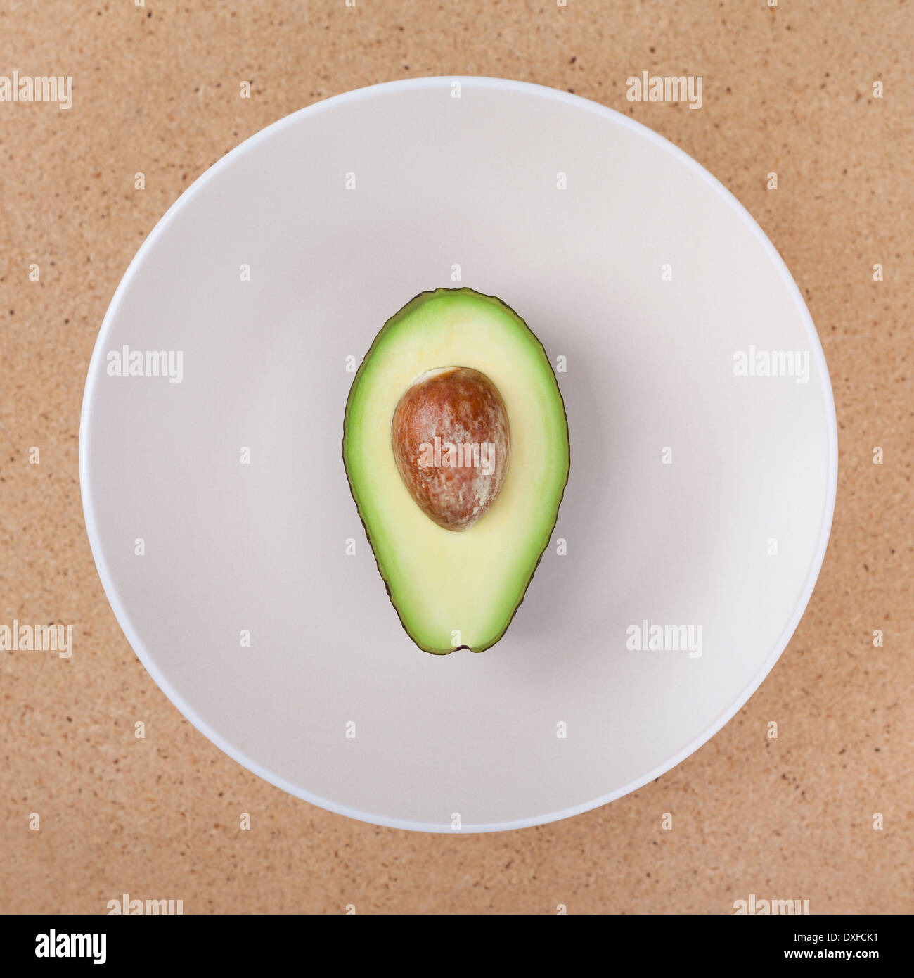 Fresche tagliate a metà di avocado con seme sulla piastra, su sfondo di legno. Foto Stock