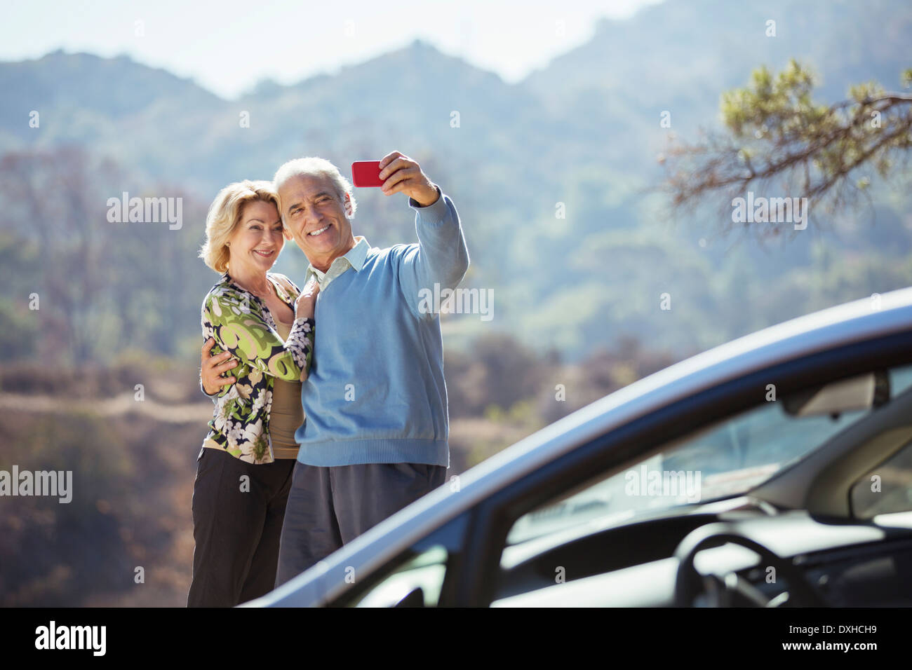 Coppia senior tenendo autoritratto con telefono cellulare fuori dall'auto Foto Stock