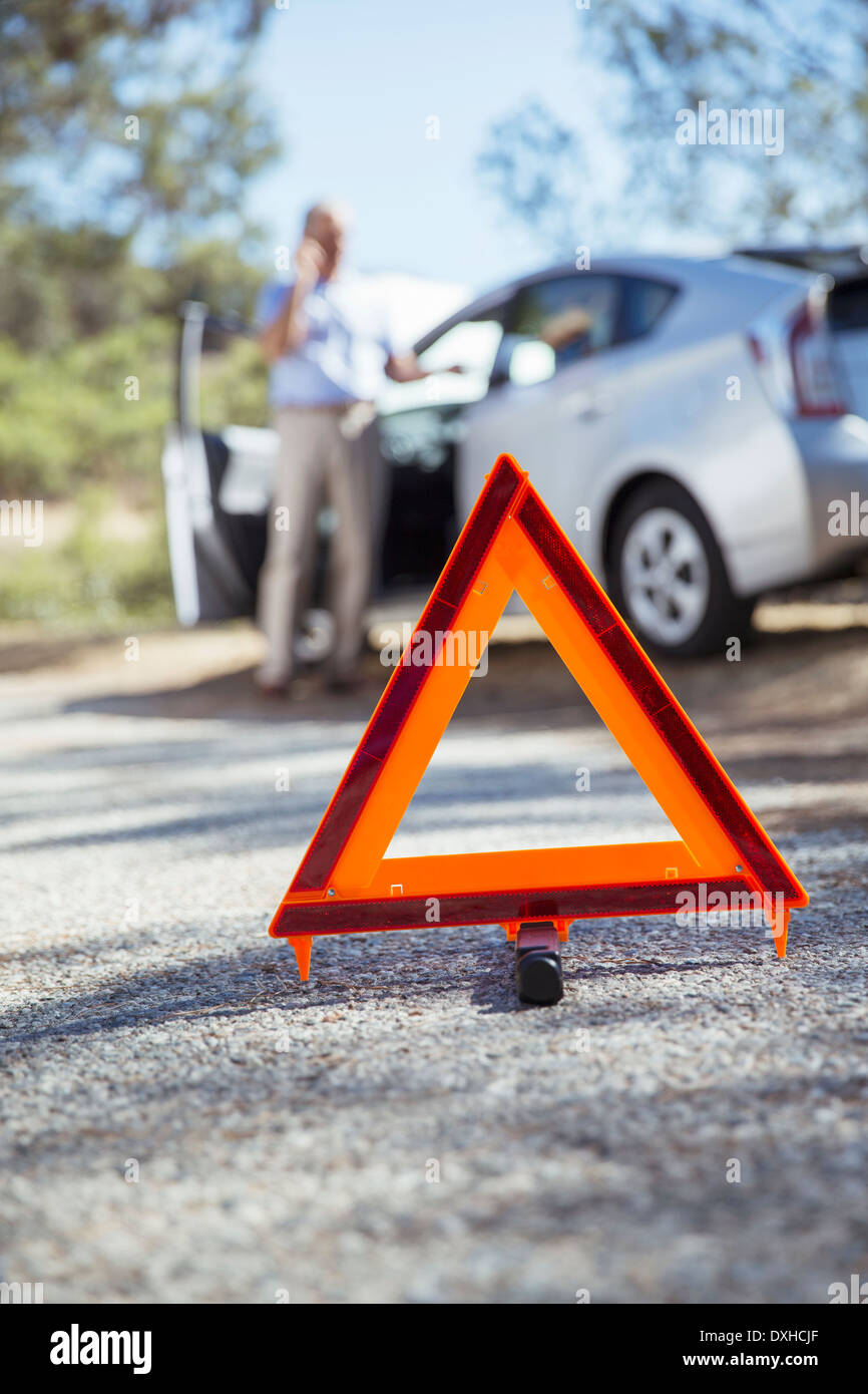 L'uomo parlando al cellulare in strada dietro il triangolo di avvertenza Foto Stock